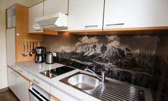 A modern kitchen with wooden and gray elements. The wall is decorated with an impressive mountain motif.