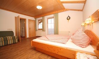 A cozy bedroom with a wooden ceiling and double bed. There is a comfy seating area and large windows with curtains.