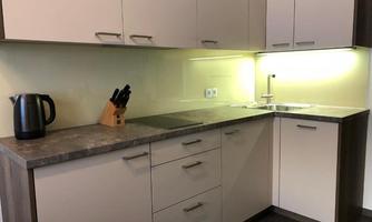 A modern kitchen with a stone countertop and light cabinets. It is well equipped with a kettle and kitchen utensils.