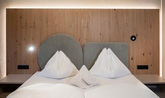 A modern bedroom with a wooden panel and two elegant headboards. The beds are decorated with white pillows and blankets.