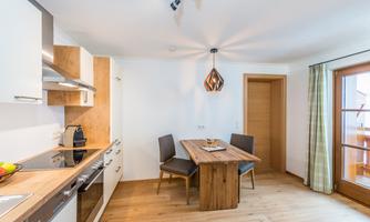 Modern kitchen with wooden details and a dining area. Large windows provide plenty of daylight.
