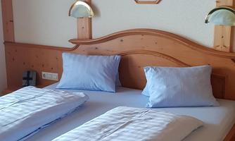 A cozy bedroom with a wooden bed and two pillows. The walls and ceiling are made of wood, creating a warm atmosphere.