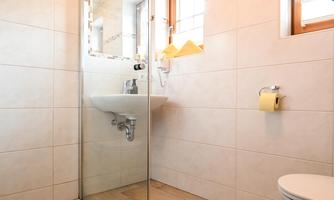 A modern bathroom with a glass shower and bright tiles. There is a sink and a window that lets in daylight.