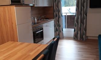 A modern kitchen with wooden details and a dining table. In the background, there is a window with a view of nature.