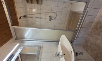 A modern bathroom with a shower cabin and a sink. The walls are tiled with white tiles and the wooden ceiling creates a cozy atmosphere.