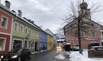 A picturesque street with colorful houses and a beautiful church tower. The ground is covered with snow and the sky is overcast.