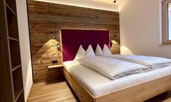 A modern bedroom with a wooden bed and a warm, inviting atmosphere. The walls are partially made of wood and the lighting is cozy.