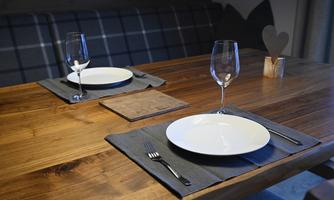 A beautifully set wooden dining table with two plates and wine glasses. The tablecloth is made of gray fabric, and there is a decorative wooden figure in the shape of a heart.