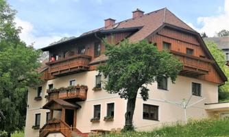 A charming house with wooden cladding and balconies. Surrounded by a green meadow and trees.