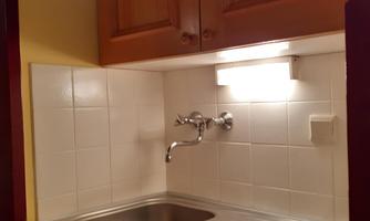 A small kitchen with a sink and two cooking burners. The walls are brightly tiled and wooden cabinets provide storage space.