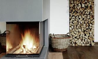 A modern fireplace with a flaming fire in a cozy room. Next to the fireplace stands a woodpile and two baskets.