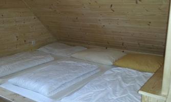 A cozy bedroom with a wooden bed and several pillows. The walls and ceiling are made of light wood, creating a warm atmosphere.