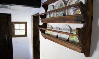 A rustic wooden shelf with colorful plates hangs on the wall. In the background, a small window can be seen.