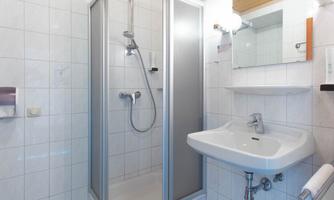 A modern bathroom with a shower cubicle and a sink. The walls are tiled and the space appears clean and bright.