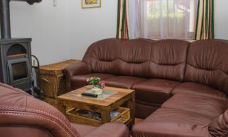 A cozy living room with a brown leather sofa and a wooden table. In the background, there is a tiled stove and some decorative elements on the wall.