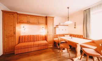 A cozy living area with wooden furniture and a dining table. The warm colors create an inviting atmosphere.
