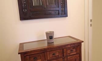 An elegant wooden table stands against the wall, and above it hangs an intricately decorated wall panel. On the table, there is a small vase.