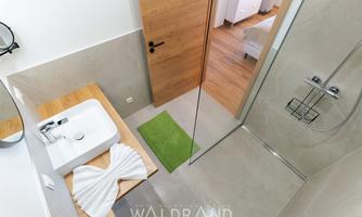 A modern bathroom with a shower and a sink. The floor is fitted with gray tiles and a green carpet.