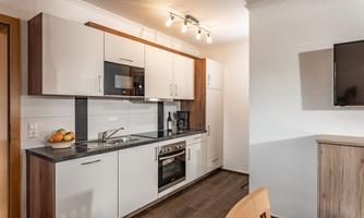 A modern kitchen with white cabinets and wood accents. It is equipped with a stove, a microwave, and a refrigerator.