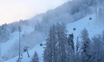 A snowy winter landscape with gentle hills and ski lifts. The forest is surrounded by frosty fog.