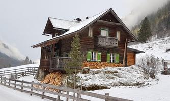 A picturesque wooden house in the midst of a snowy landscape. Surrounded by trees and a fence, it appears inviting and cozy.