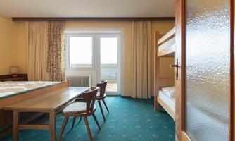A simple room with a table, two chairs, and a bunk bed.  
A lot of light comes into the room through large windows.
