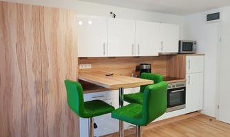 A modern kitchen with a table and green bar stools. The decor is bright and cheerful, featuring wood and white elements.