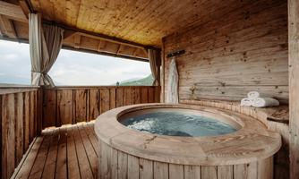A cozy wooden jacuzzi in a cabin with a view of the mountains. The wooden paneling and the soft towels create a relaxing atmosphere.