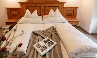 A cozy bedroom with a large bed and wooden details. On the bedspread lies an open book and a wool blanket.