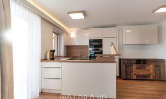 Modern kitchen with wood finishes and elegant white cabinets. Large windows provide plenty of daylight.