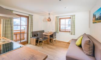 A bright and modern apartment with wooden flooring and large windows. The living area is cozily furnished with a dining table and a comfortable couch.
