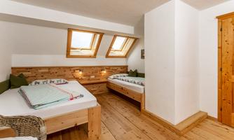 A cozy bedroom with two single beds and a double bed. Bright walls and wooden paneling create a warm atmosphere.