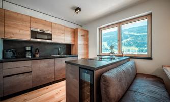 A modern kitchen with wooden cabinets and an elegant countertop. Large windows offer a view of nature.