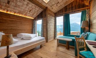 A cozy room with wooden paneling and large windows that offer a view of the mountains. The decor is stylish and modern, featuring a bed and a small seating area.