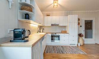 A modern, bright kitchen with white cabinets and a wooden countertop. On the counter, there is a coffee machine and a kettle.