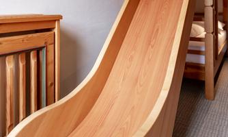 A slide made of wood is in a children's room. In the background, bunk beds can be seen.