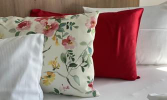 A cozy bedding set with various pillows, including a floral one and a red one. The background is a light wood paneling.