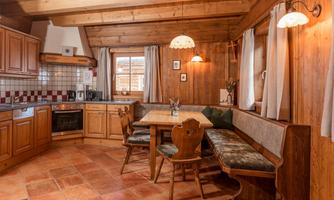 A cozy kitchen in rustic style with wooden cabinets and a seated dining group. Plenty of daylight pours through the windows, creating an inviting atmosphere.
