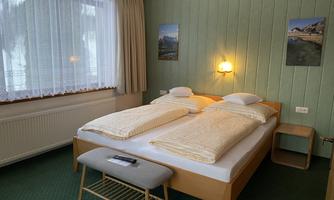 A cozy bedroom with a double bed and two pillows. The walls are painted green, and a window provides natural light.