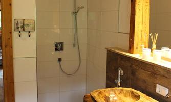A modern bathroom with a wooden sink and a spacious shower area. The decor is bright and inviting, featuring natural materials.