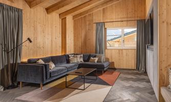 A modern living room with wooden walls and a large window front. A comfortable couch and a stylish table create a cozy atmosphere.