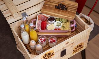 A wooden box with breakfast ingredients, including bottles of milk, eggs, fruit, and cold cuts. The presentation is appealing and inviting.