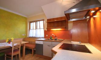 A modern kitchen with light green walls and wooden details. The room is well-lit and has a dining area with a table and chairs.