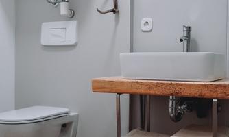 A modern bathroom with a toilet and sink. Wooden shelves contain folded towels.