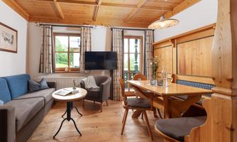 A cozy living space with wood decor, a blue sofa, and a dining table. Large windows provide plenty of natural light and an inviting atmosphere.
