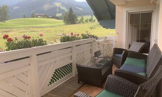 A cozy balcony with rattan furniture and a view of a green landscape. In the background, gentle hills and trees can be seen.