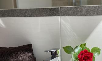 A modern bathroom with a faucet, a towel, and a small vase with a red rose. The furnishings appear elegant and inviting.