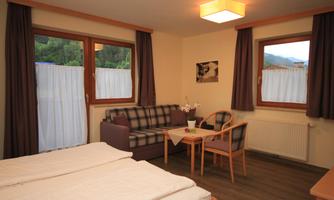A cozy room with two beds, a sofa, and a table.  
Bright windows offer a view outside and provide plenty of daylight.