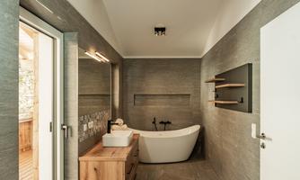 A modern bathroom with a freestanding bathtub and a wooden dresser. Large windows provide plenty of daylight.