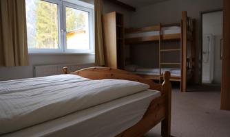A simple youth room with two single beds and a bunk bed. There is a window with a view and practical furnishings.